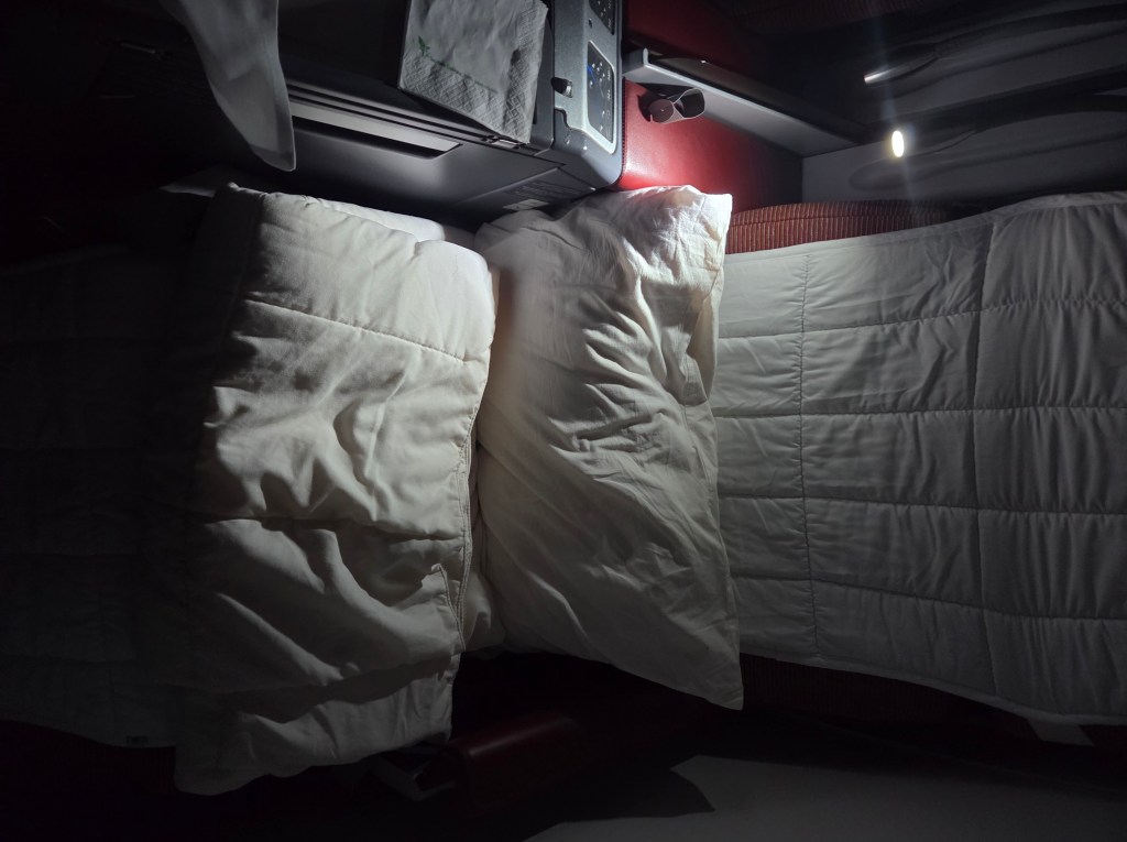 Seat in "bed mode" with mattress pad, duvet, and pillow